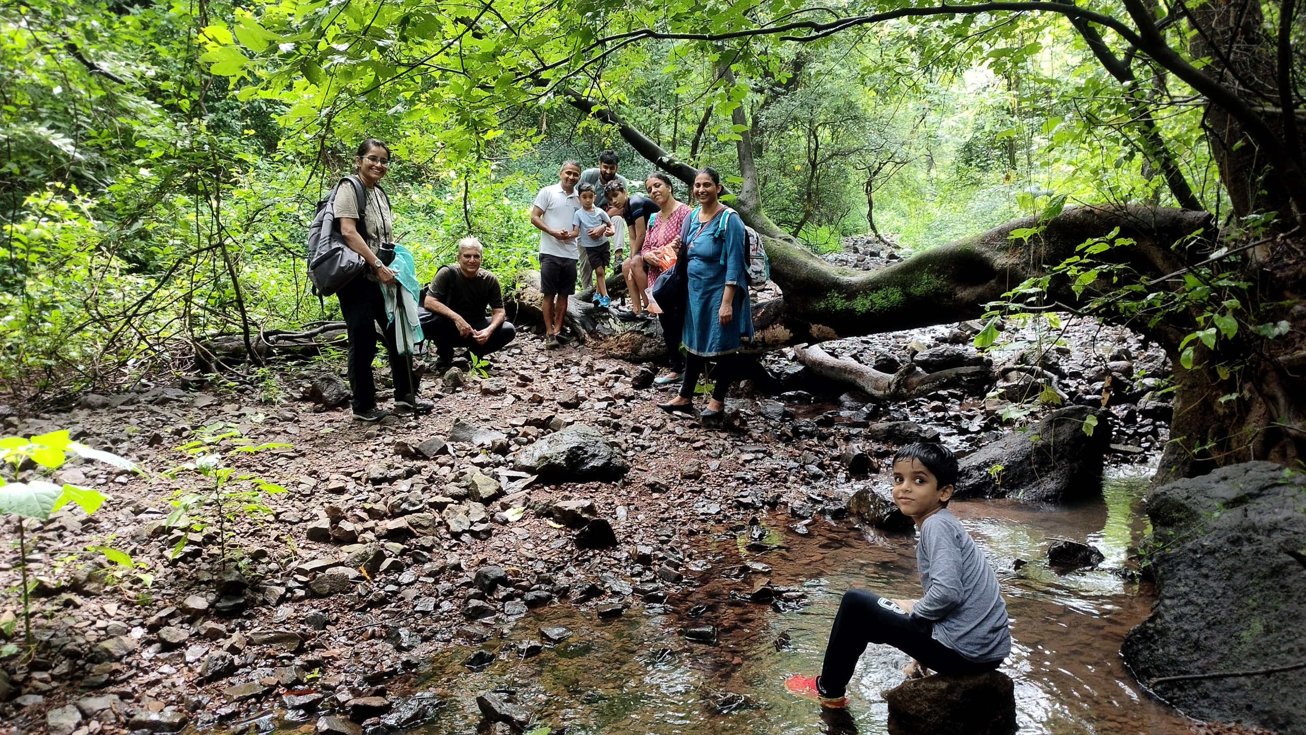 Kids and adults posing along side a fallen tree and stream of water at CEC BNHS